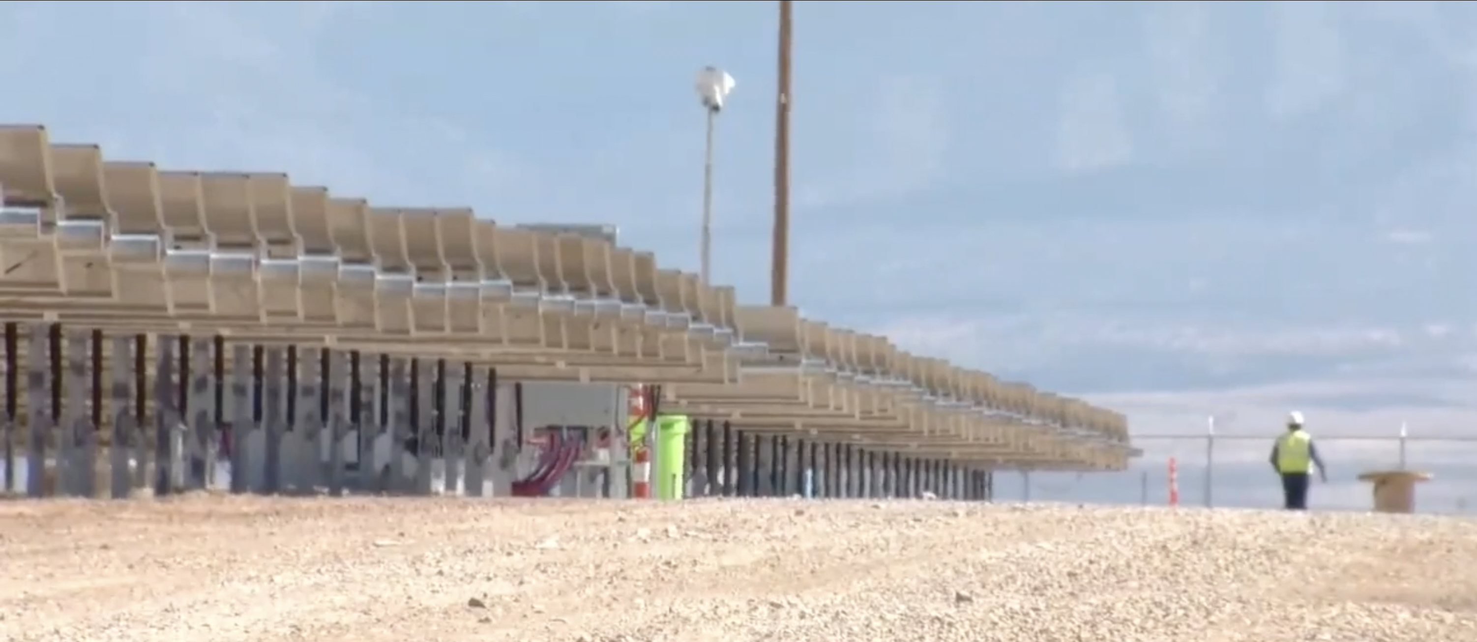 Rows of single‑axis trackers at the Belen community solar project with an installer walking the line